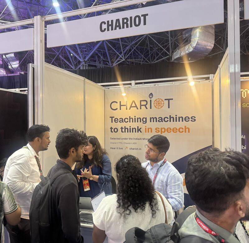 Visitors talking with the Chariot team at the booth, under the line “Teaching machines to think in speech”